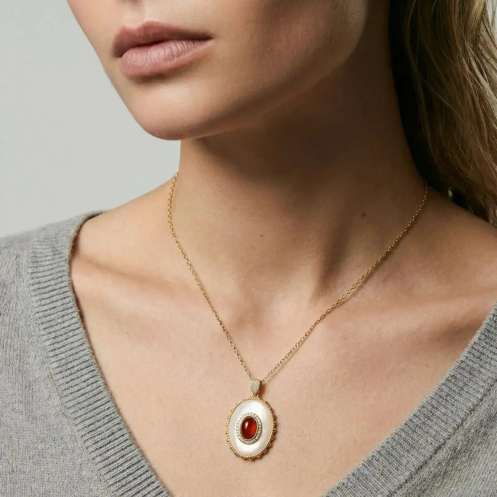 Woman wearing gold chain with oval cameo pendant featuring red gemstone center
