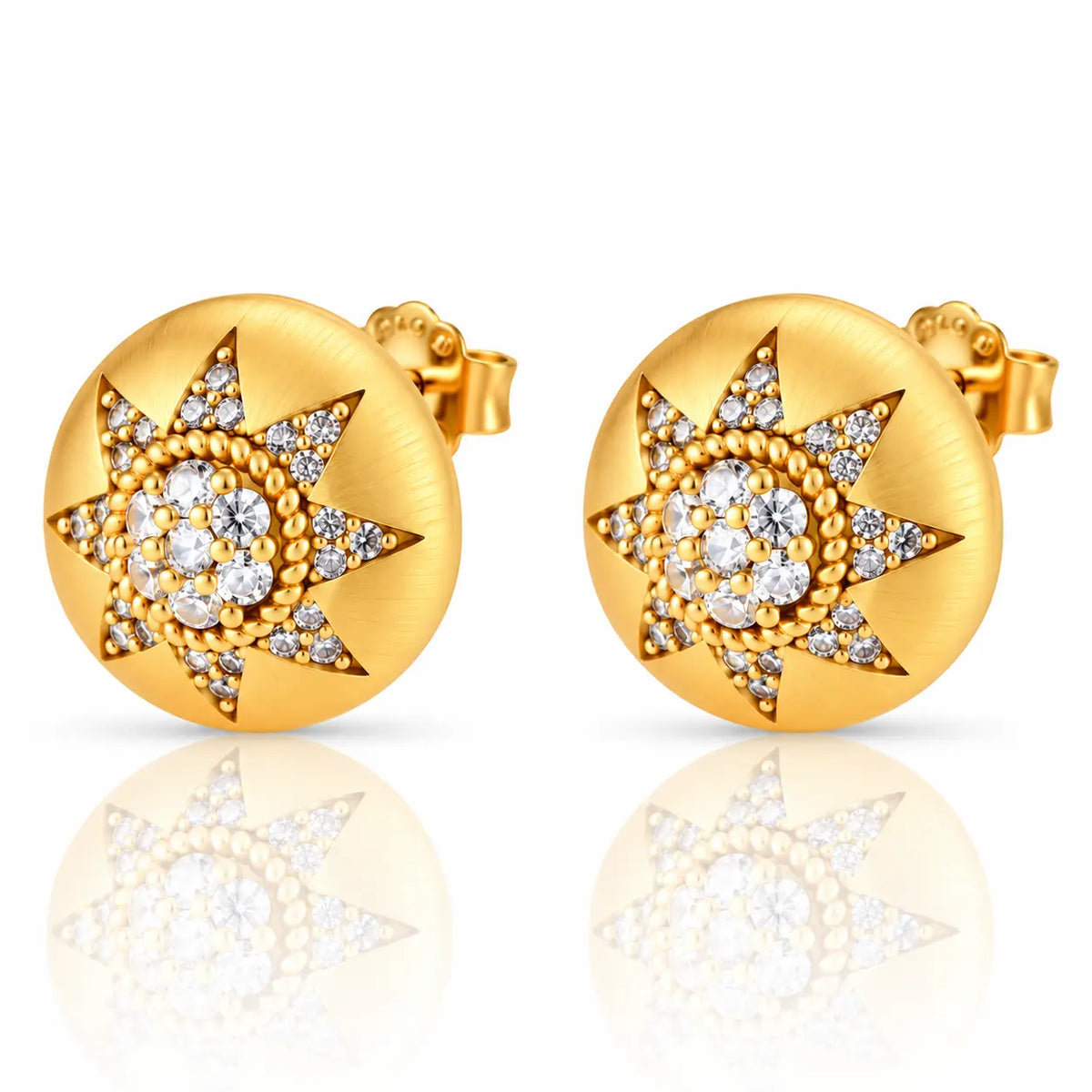 A pair of round gold stud earrings with a starburst design set with clear gemstones, shown on a white background with a soft reflection below.
