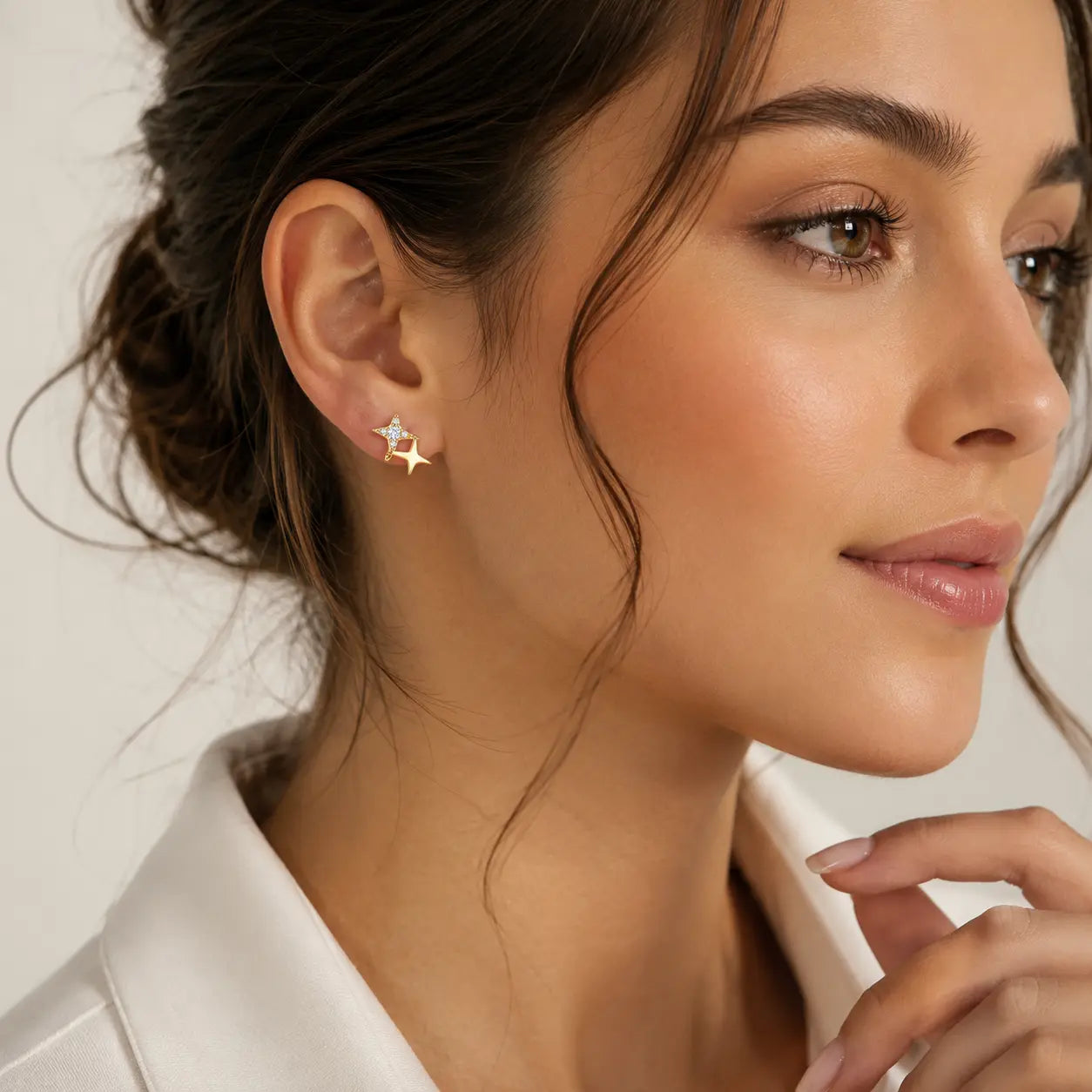 A close-up of a woman wearing a small gold star-shaped stud earring, shown from the side against a soft light background.