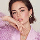 Woman wearing gold hoop earrings and a necklace, sitting on a pink fluffy surface.