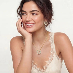 Woman wearing gold jewelry including a necklace and earrings on a plain background