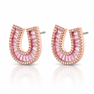 A pair of rose gold horseshoe-shaped stud earrings embellished with pink baguette-cut crystals and small clear stones, shown on a white background with a soft reflection.