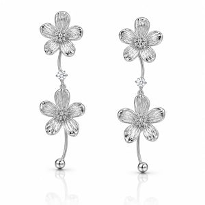 A pair of silver dangle earrings featuring textured five-petal flower charms with small clear stones in the centers, connected by curved stems with bead ends, shown on a white background with a soft reflection.