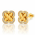 A pair of gold post earrings with a four-leaf clover shape, featuring a braided knot design in the center and a border of small clear stones, shown on a white background with a reflection.