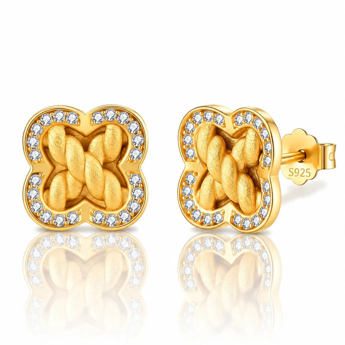 A pair of gold post earrings with a four-leaf clover shape, featuring a braided knot design in the center and a border of small clear stones, shown on a white background with a reflection.