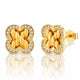 A pair of gold post earrings with a four-leaf clover shape, featuring a braided knot design in the center and a border of small clear stones, shown on a white background with a reflection.