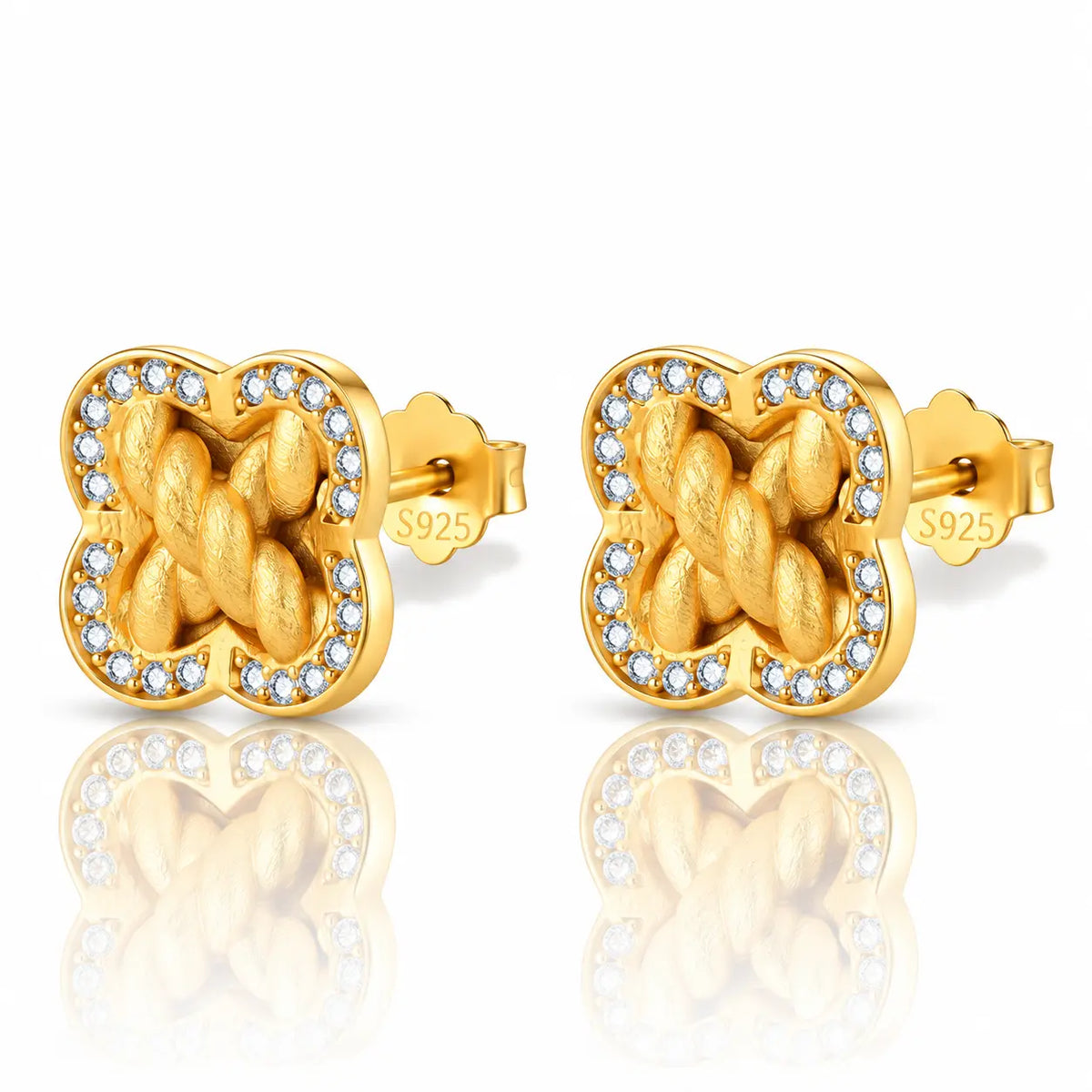 A pair of gold-toned stud earrings with a four-leaf clover shape, featuring a twisted knot design in the center and a border of small clear stones, shown on a white background with a soft reflection below.