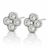 A pair of diamond stud earrings in a four-petal flower setting, crafted in silver-toned metal with a central pearl-like bead, shown on a reflective white surface.