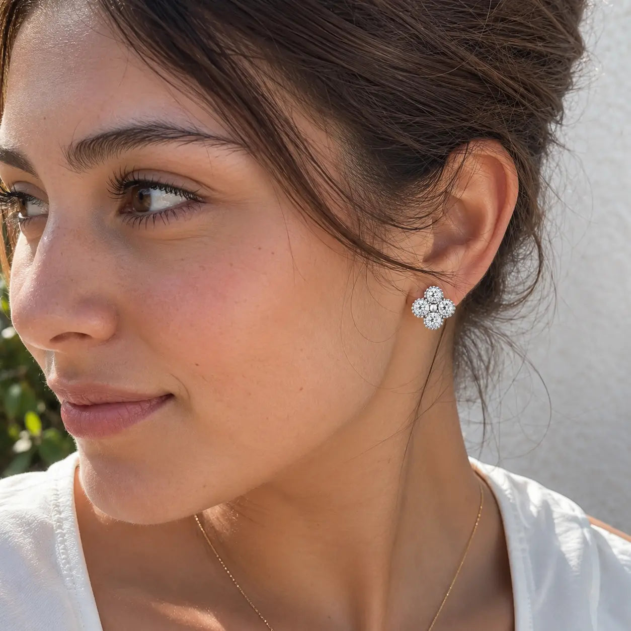 A close-up of a woman wearing a silver-toned four-petal flower stud earring, shown from the side against a light neutral background.