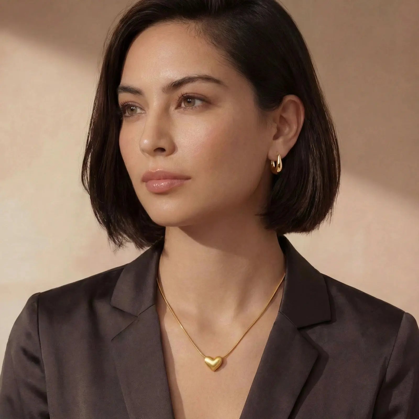 Woman wearing a gold necklace with a heart pendant against a beige background