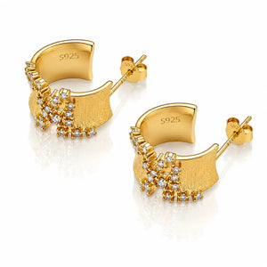 A pair of gold crescent-shaped hoop earrings with textured and polished sections, decorated with small clear crystal clusters, shown on a white reflective background. The inside of the hoops is stamped with 'S925'.