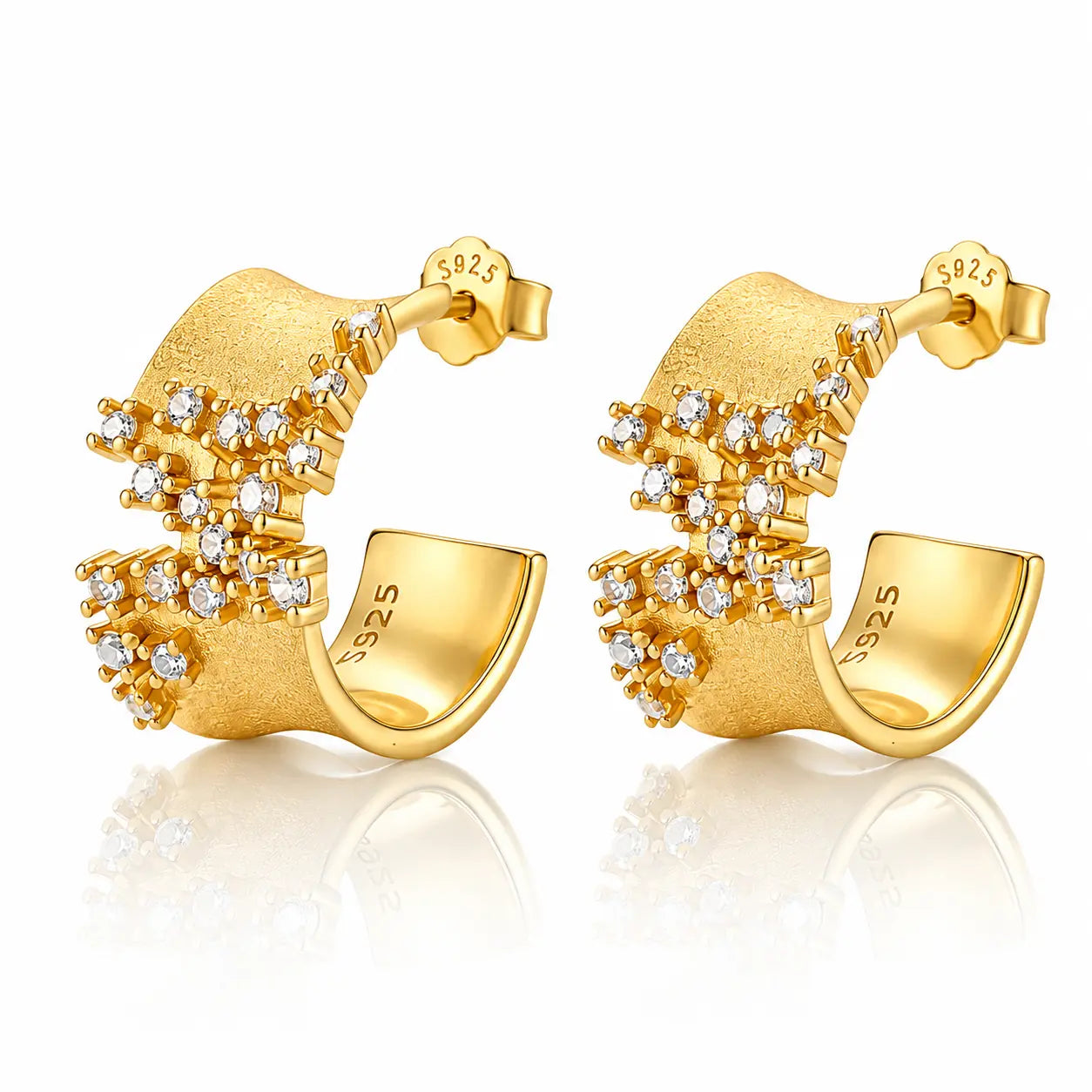 A pair of gold geometric stud earrings with clear gemstones, displayed on a clean white background with a soft reflection below.