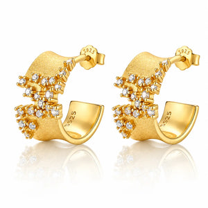 A pair of gold geometric stud earrings with clear gemstones, displayed on a clean white background with a soft reflection below.