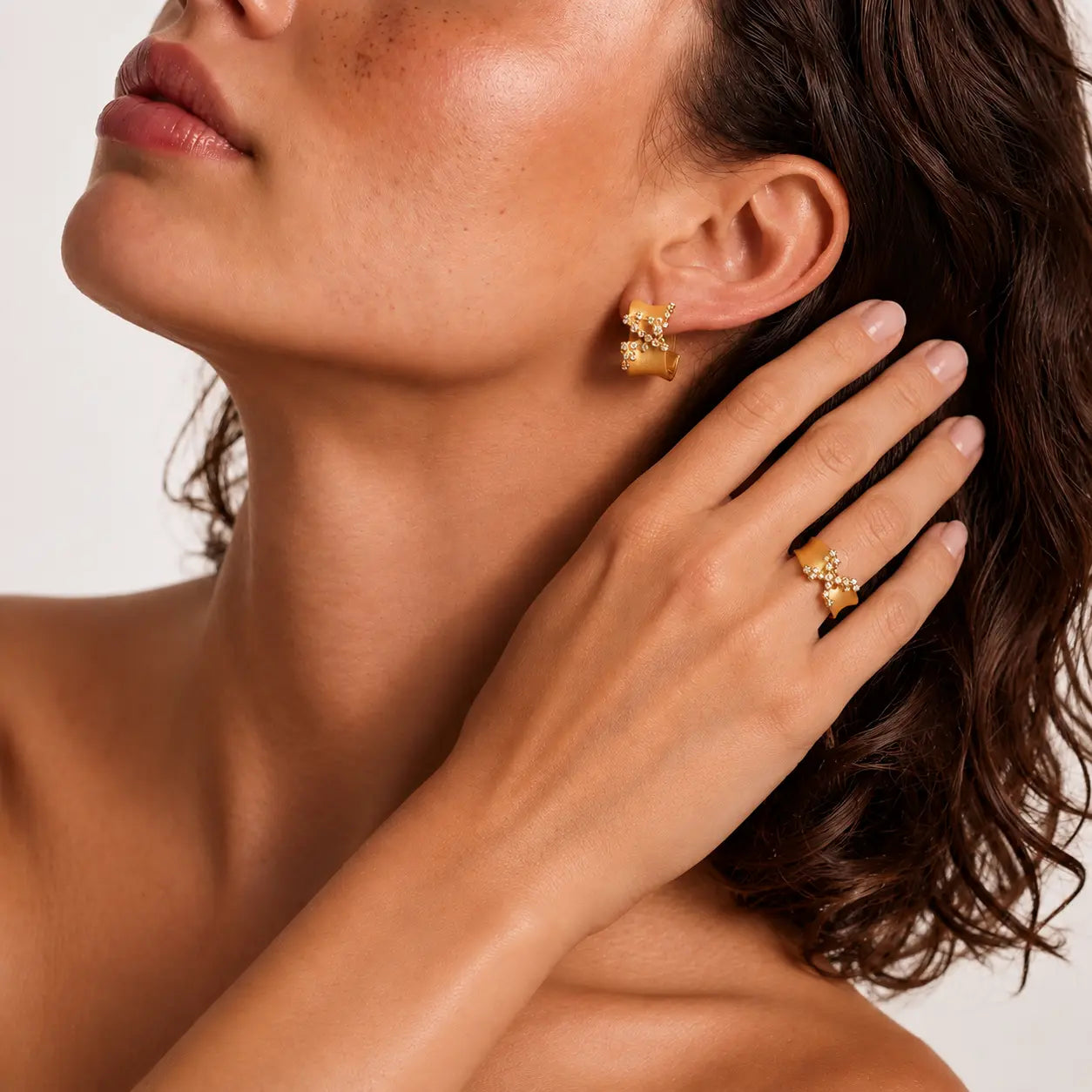 Close-up of a model wearing gold jewelry, including a delicate gold chain necklace with a small gold pendant, gold hoop earrings, and a gold headband, against a clean white background.