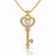 A gold key-shaped pendant necklace adorned with clear pavé stones and a heart-shaped clear center stone, suspended from a gold chain on a white background with a soft reflection below.