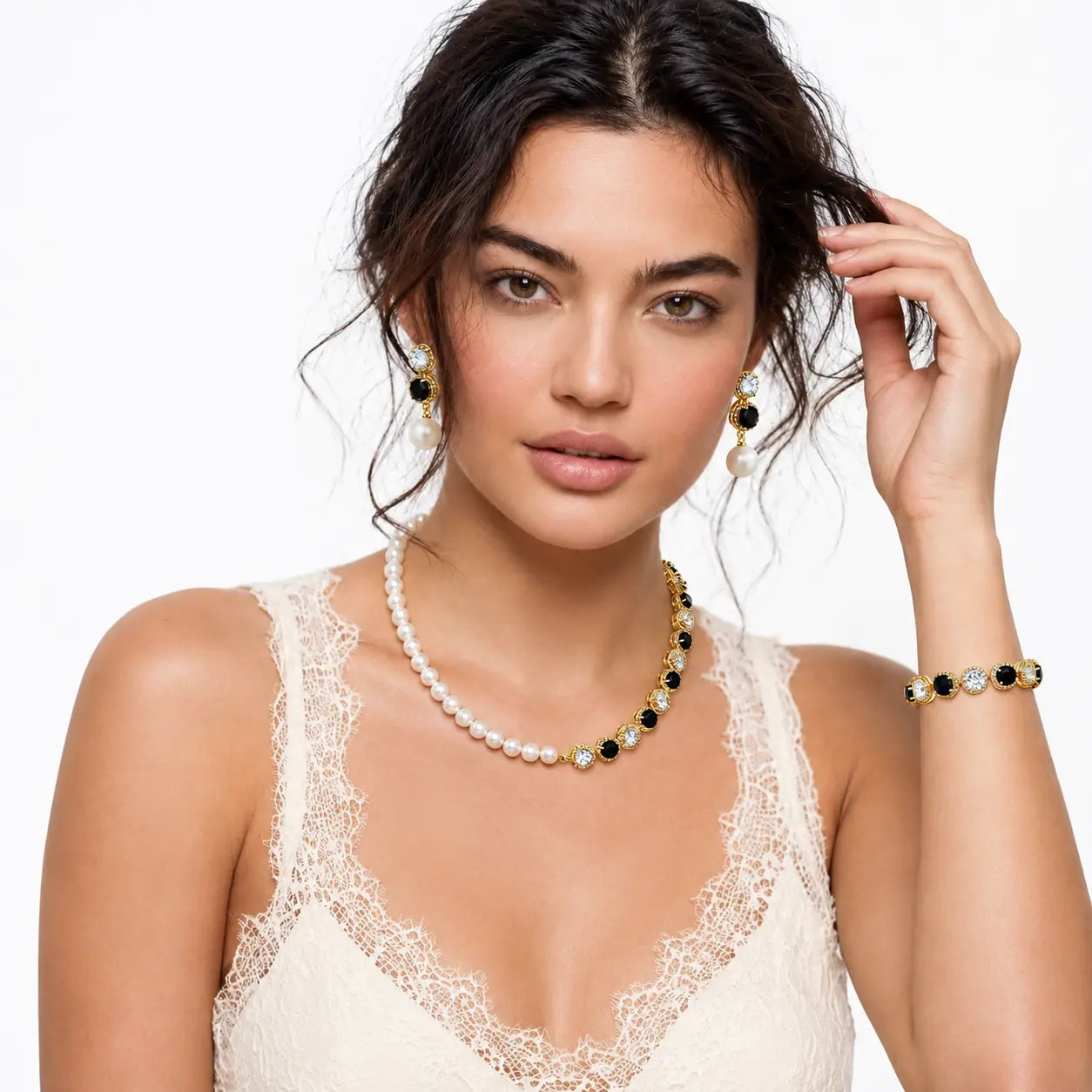 A woman modeling a matching jewelry set featuring a pearl and black stone necklace, matching drop earrings, and a bracelet with white pearls, gold settings, and green stones, against a plain white background.