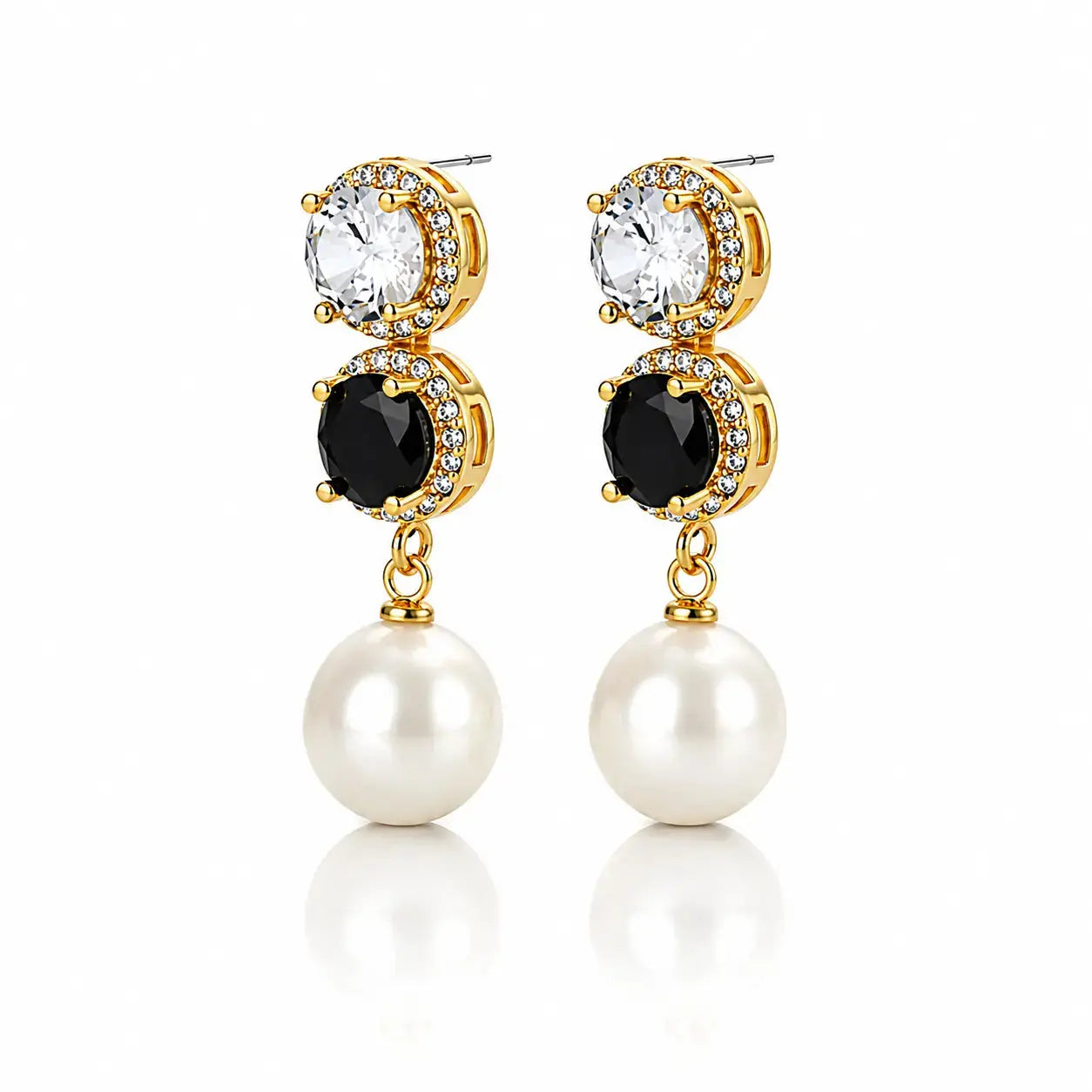 A pair of gold drop earrings featuring a clear round crystal, a black round crystal surrounded by small clear stones, and a dangling white pearl, shown on a white background with a soft reflection.