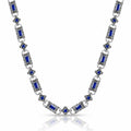 A silver-toned link necklace featuring rectangular blue gemstones and small blue floral accents, displayed on a clean white background with a soft reflection below.