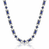 A silver-toned link necklace featuring rectangular blue gemstones and small blue floral accents, displayed on a clean white background with a soft reflection below.