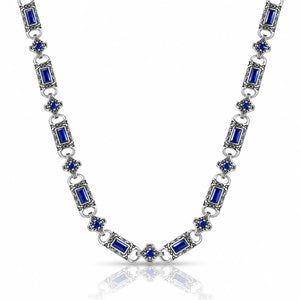A silver-toned link necklace featuring rectangular blue gemstones and small blue floral accents, displayed on a clean white background with a soft reflection below.