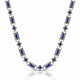 A silver-toned link necklace featuring rectangular blue gemstones and small blue floral accents, displayed on a clean white background with a soft reflection below.
