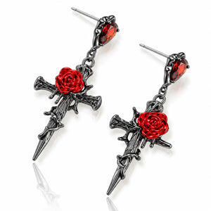 A pair of gothic dangle earrings featuring blackened metal dagger crosses with vibrant red rose engravings and red faceted crystal studs at the top, displayed on a clean white background with a soft reflection.