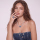 Woman wearing a blue butterfly ring and necklace against a light pink background