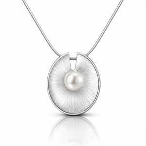 A silver pendant necklace featuring a brushed circular disc with a single white pearl at its center, suspended from a fine silver chain on a white background with a soft reflection below.