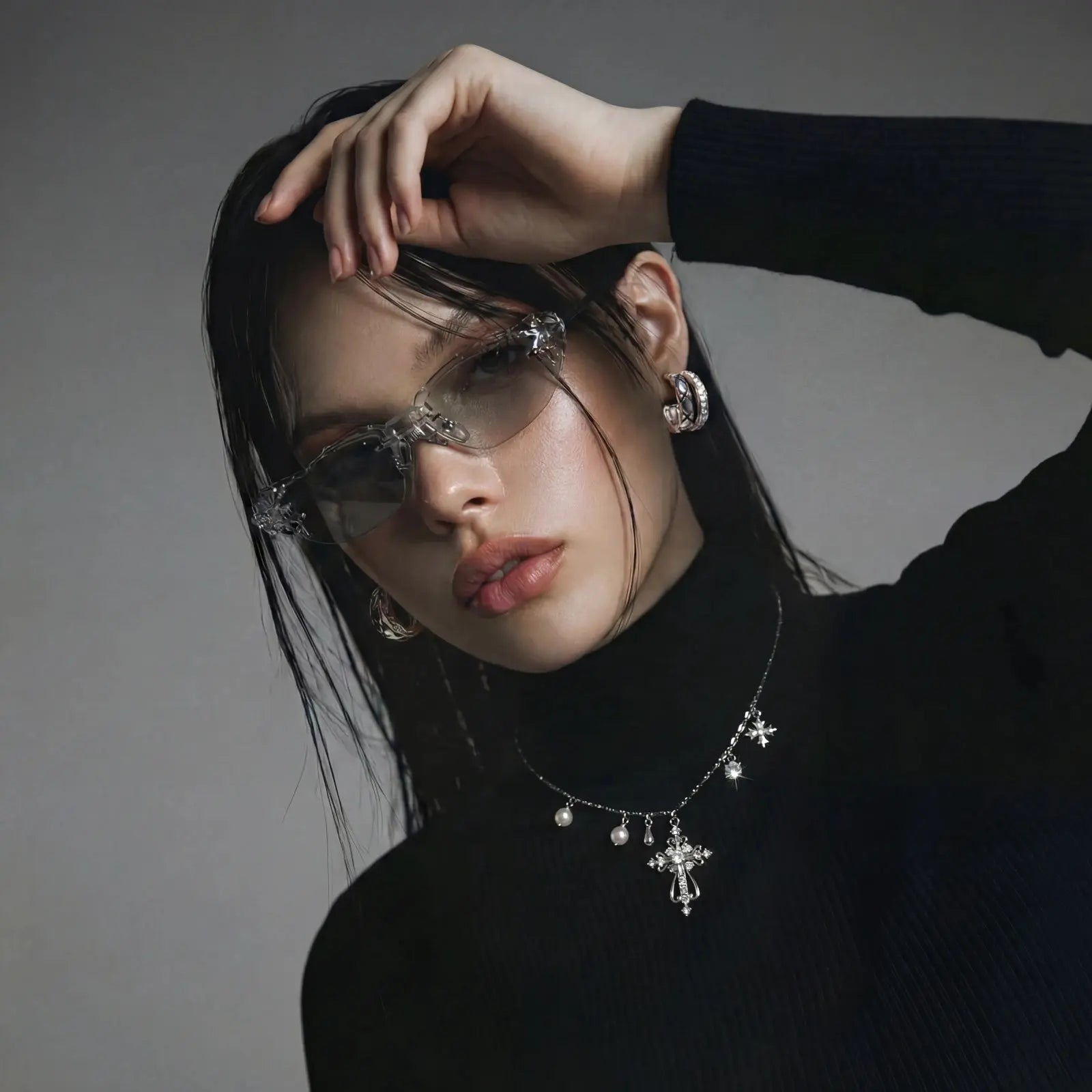 Person wearing a black turtleneck and silver jewelry against a gray background