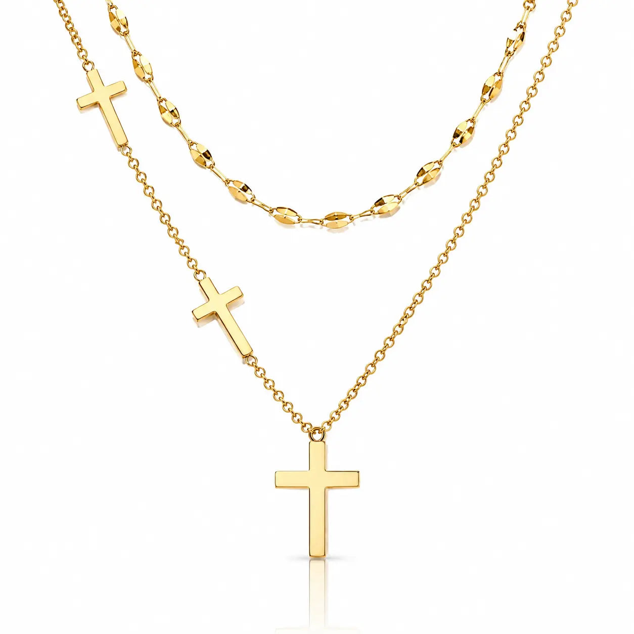 A gold layered necklace set on a white background, featuring a short chain with a small cross, a longer chain with a larger cross pendant, and a beaded chain in the back.