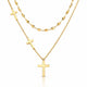 A gold layered necklace set on a white background, featuring a short chain with a small cross, a longer chain with a larger cross pendant, and a beaded chain in the back.