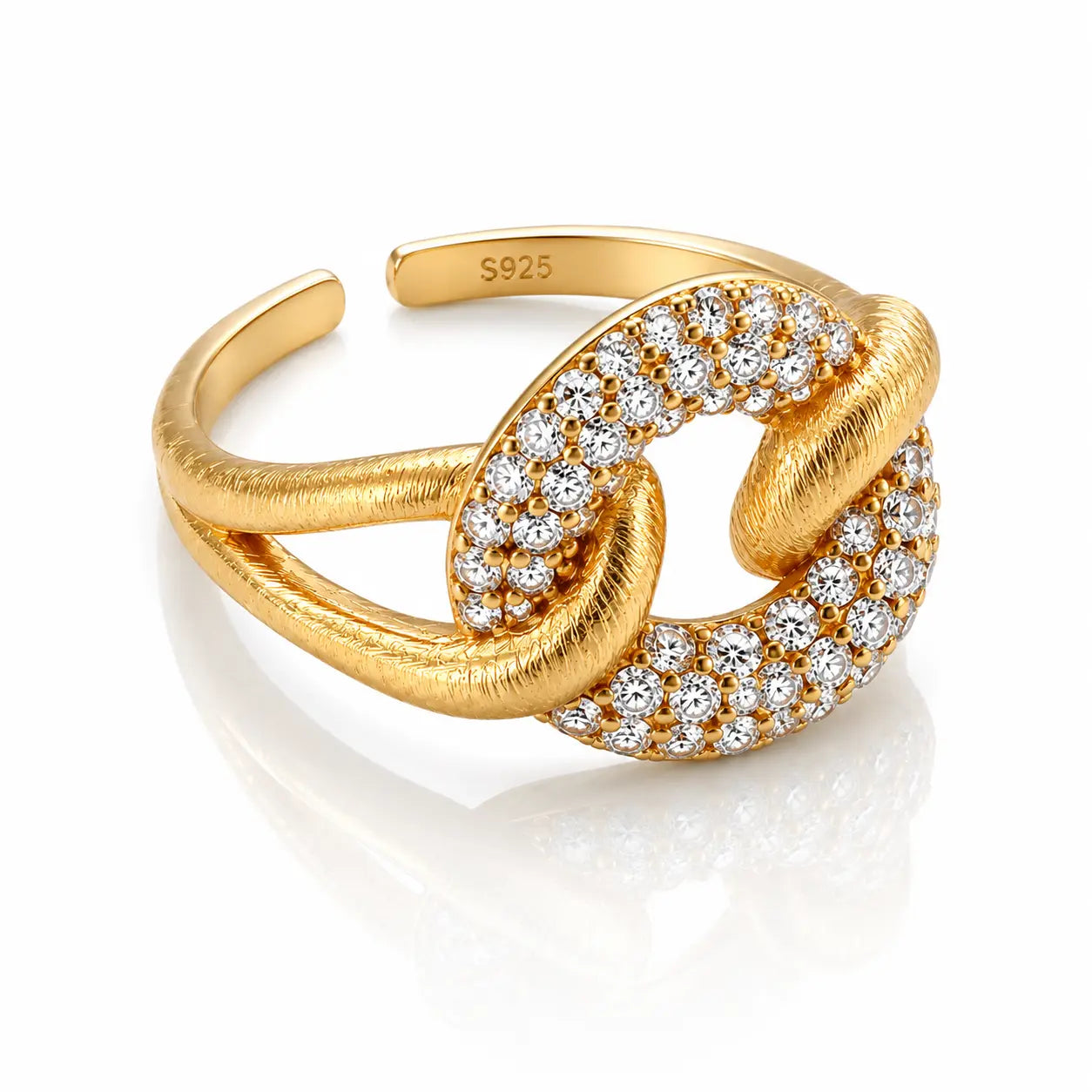 A gold adjustable ring featuring a knot-like design with pavé-set clear stones on one side and a textured finish on the other, shown on a white reflective background.
