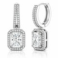 A pair of silver-toned huggie hoop earrings with rectangular princess-cut diamond drops, surrounded by halo and channel settings of small round diamonds, shown on a white background with a subtle reflection.