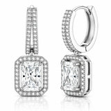 A pair of silver-toned huggie hoop earrings with rectangular princess-cut diamond drops, surrounded by halo and channel settings of small round diamonds, shown on a white background with a subtle reflection.