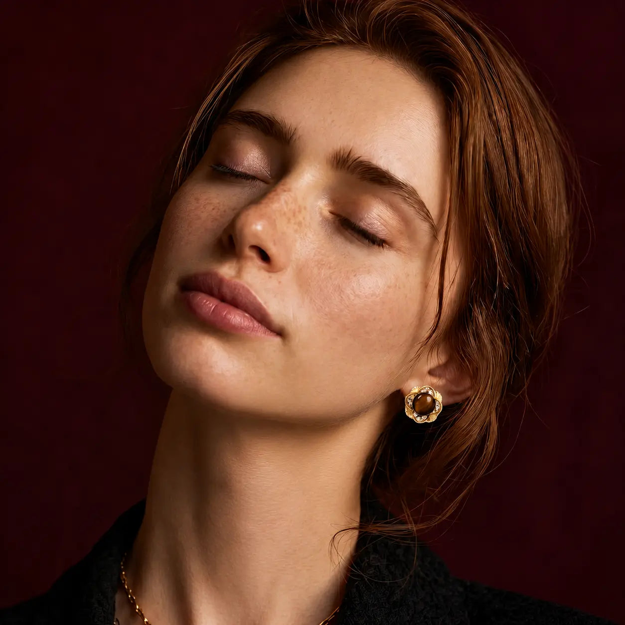 Close-up of a woman with closed eyes wearing gold earrings against a dark background