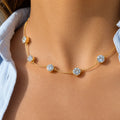 A delicate gold chain necklace with five round-cut clear gemstones spaced evenly, worn on a model's neck with a light blue shirt collar visible.