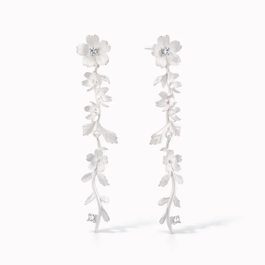 Silver drop earrings with floral and vine design and sparkling gemstone accents on white background.