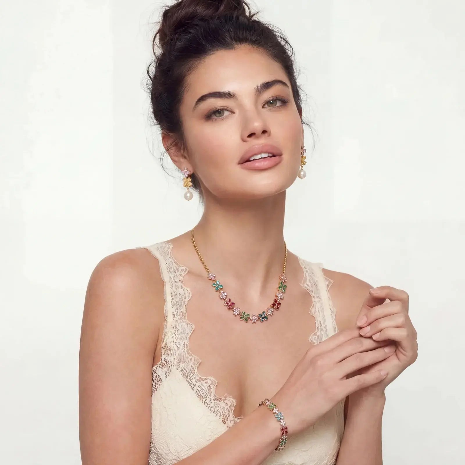 Woman wearing floral gemstone necklace, bracelet, and pearl earrings with gold accents