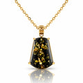 A gold pendant necklace featuring a faceted shield-shaped black stone with shimmering gold inclusions, suspended from a delicate gold chain on a white background with a soft reflection.