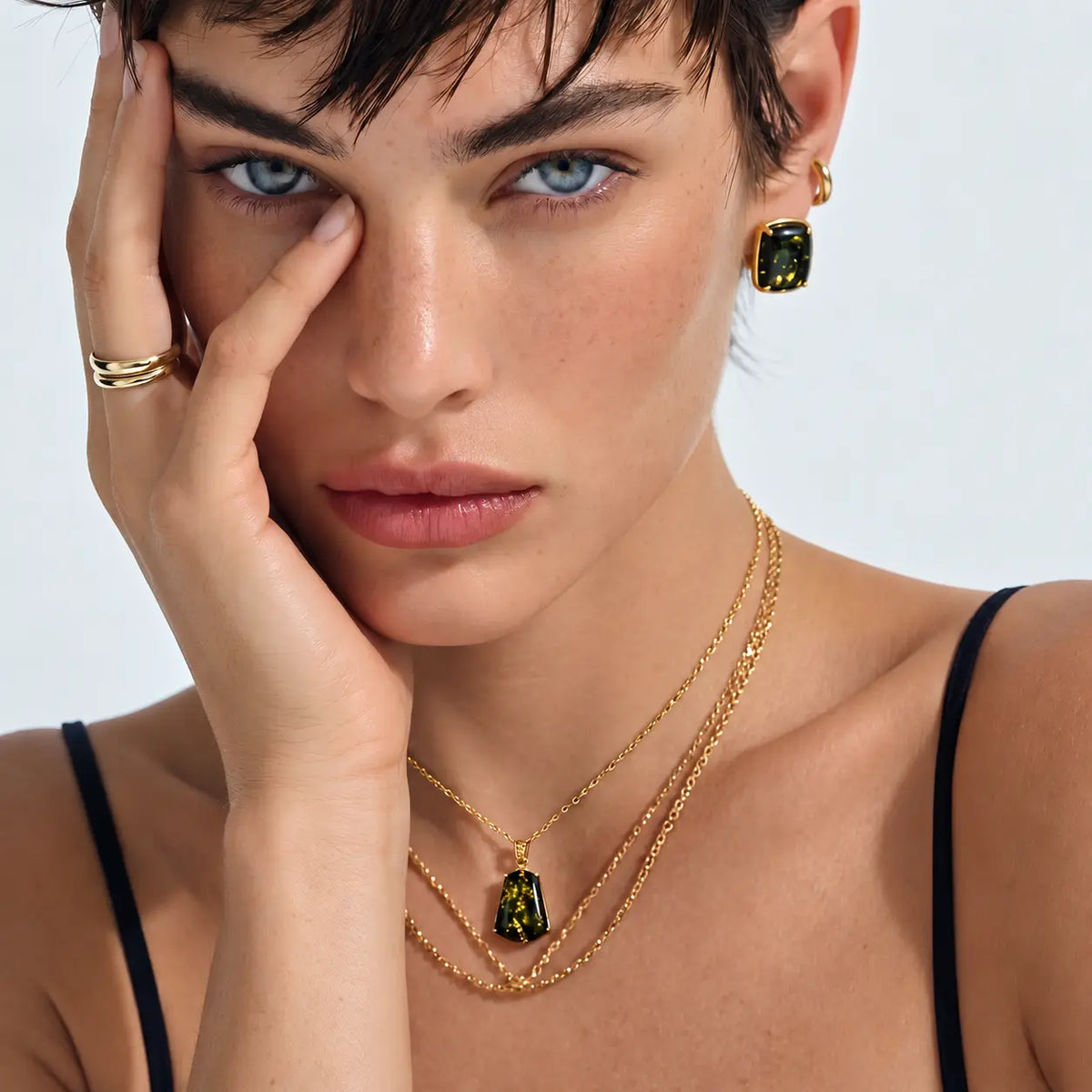 A close-up lifestyle shot of a model wearing a gold layered necklace set with green rectangular gemstone pendants and matching drop earrings.