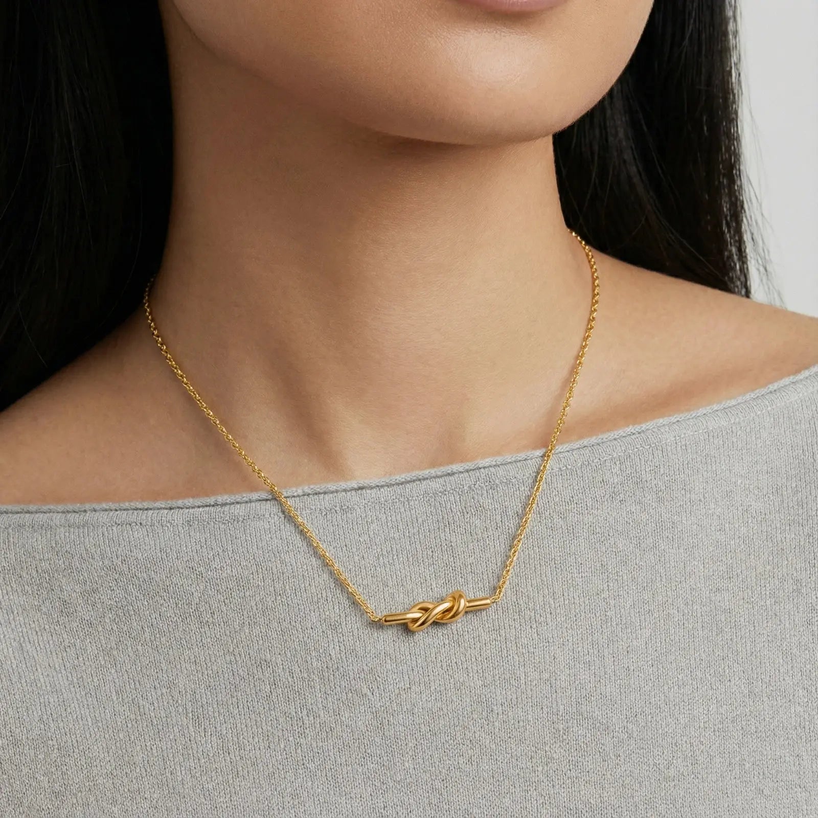 18K gold plated knot necklace on woman wearing light grey top