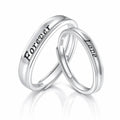 Two polished silver wedding bands interlocking on a reflective white surface. One band is engraved with the word 'Forever' and the other with 'Love'.