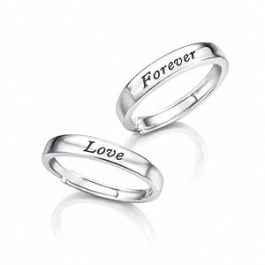Two polished silver rings on a white reflective background, one engraved with the word 'Love' and the other with 'Forever'.