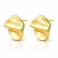 A pair of gold abstract stud earrings with a smooth, organic wavy design, displayed on a clean white background with a soft reflection below.