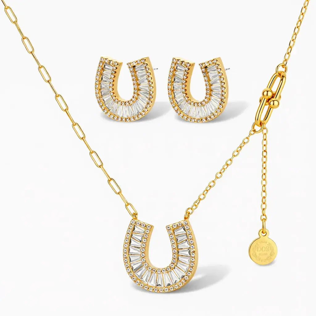 Gold horseshoe necklace and earrings set with clear baguette and pavé crystals on white background