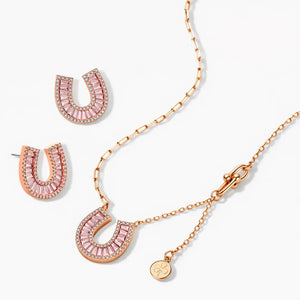 Rose gold horseshoe necklace and earrings set with pink gemstones on a white background