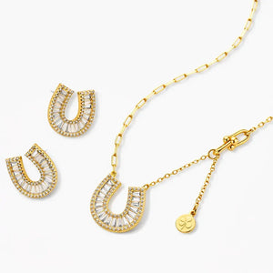 Gold horseshoe necklace and earrings set with clear baguette crystals on white background