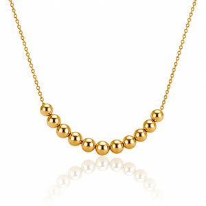 A gold beaded necklace featuring a curved row of polished spherical beads on a delicate gold chain, displayed against a clean white background with a soft reflection below.