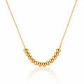 A gold beaded necklace with a curved row of polished spherical beads on a delicate chain, displayed against a clean white background with a soft reflection below.