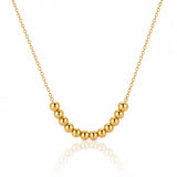 A gold beaded necklace with a curved row of polished spherical beads on a delicate chain, displayed against a clean white background with a soft reflection below.